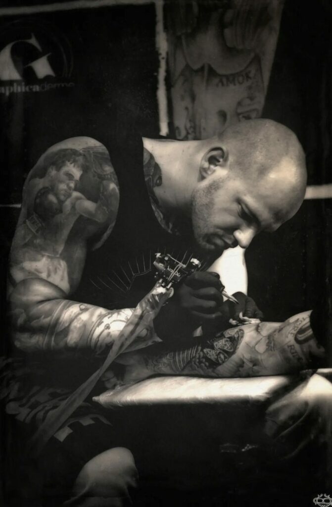 Steven Chaudesaigues, tatoueur Graphicaderme, en séance de tatouage à l’atelier — photo sépia